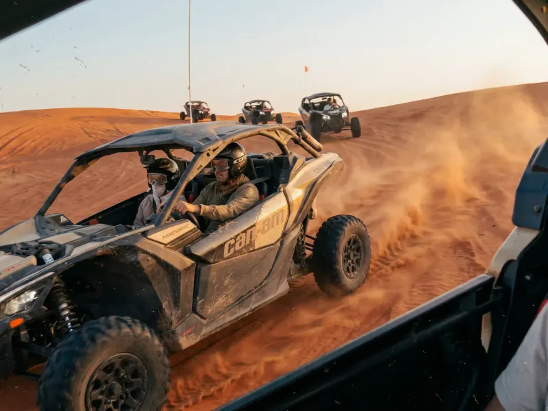 Can-Am buggies driving in convoy over red sand dunes in late-afternoon light on a dune buggy Dubai tour