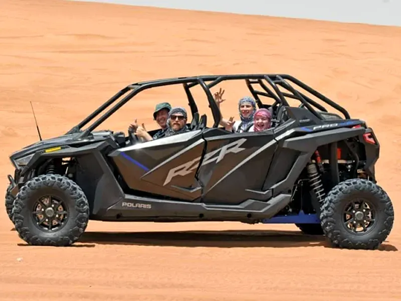 Four guests waving from a 4-seater Polaris RZR parked on red desert sand