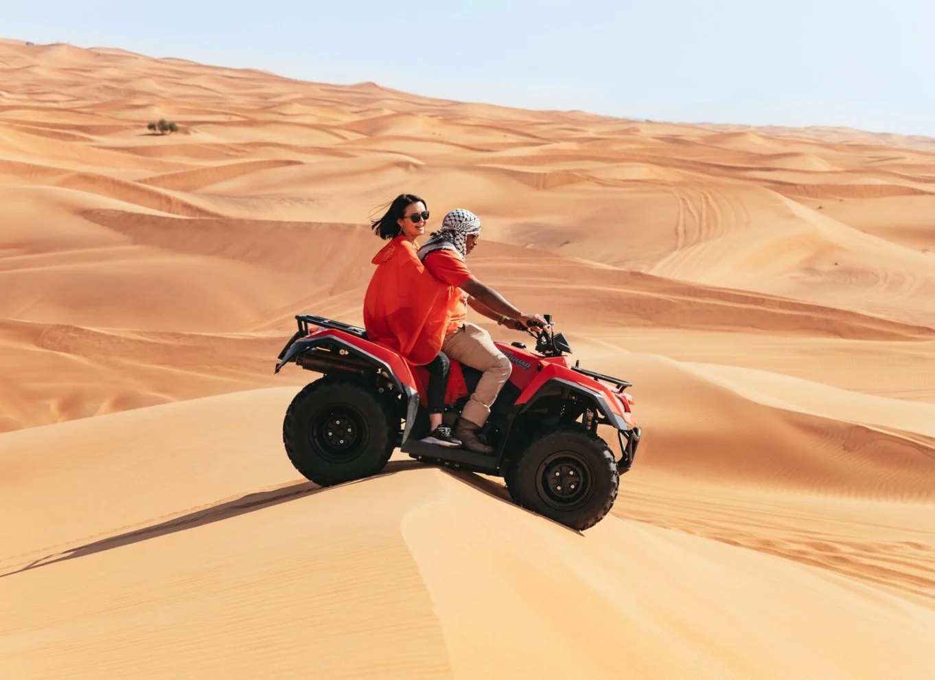 Tourists riding quad bikes across vast golden sand dunes in Dubai's Lahbab Desert under a clear blue sky