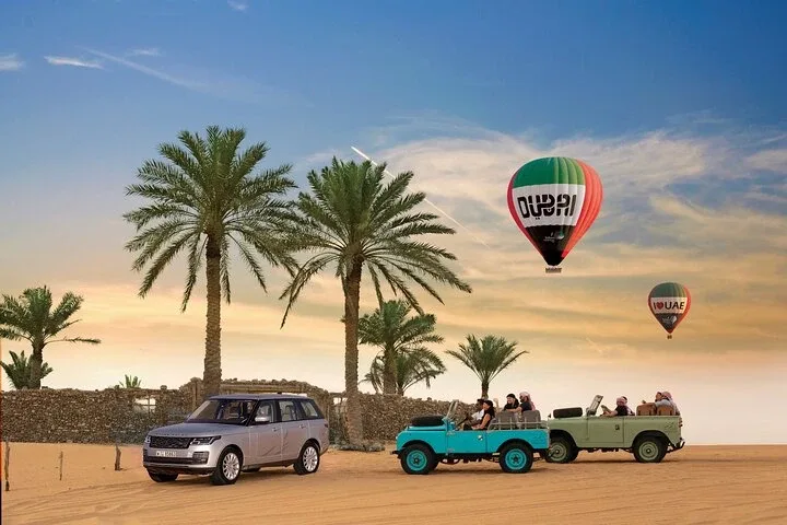 Hot air balloon with the logo 'Balloon Adventures Dubai' floating above the Dubai desert at sunrise, with other balloons in the distance