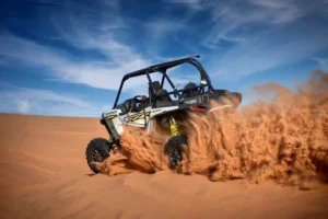 Tourists driving dune buggies across the vast desert landscape of Dubai under a clear blue sky, enjoying an adventurous and affordable experience