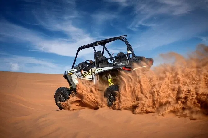 Tourists driving dune buggies across the vast desert landscape of Dubai under a clear blue sky, enjoying an adventurous and affordable experience