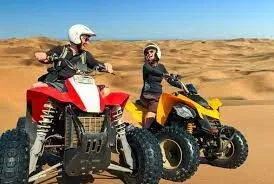 Tourists riding KTM dirt bikes across the vast, sandy Dubai desert with a guide leading the way