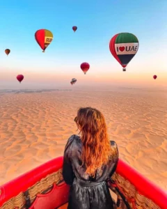 Several colorful hot air balloons floating over a vast desert landscape with hills and fields during sunset in Cappadocia