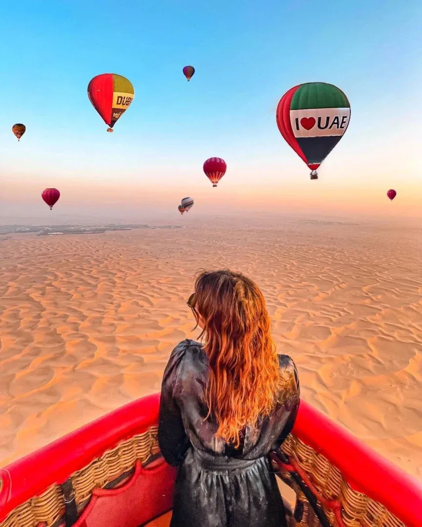 Several colorful hot air balloons floating over a vast desert landscape with hills and fields during sunset in Cappadocia