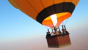 Passengers on a hot air balloon ride in a wicker basket beneath an orange and black envelope