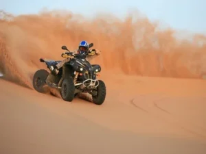 Tourists riding quad bikes across golden Dubai desert dunes, kicking up sand as they navigate the vast landscape