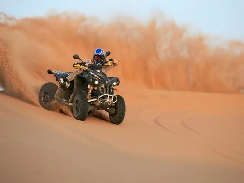Tourists riding quad bikes across golden Dubai desert dunes, kicking up sand as they navigate the vast landscape
