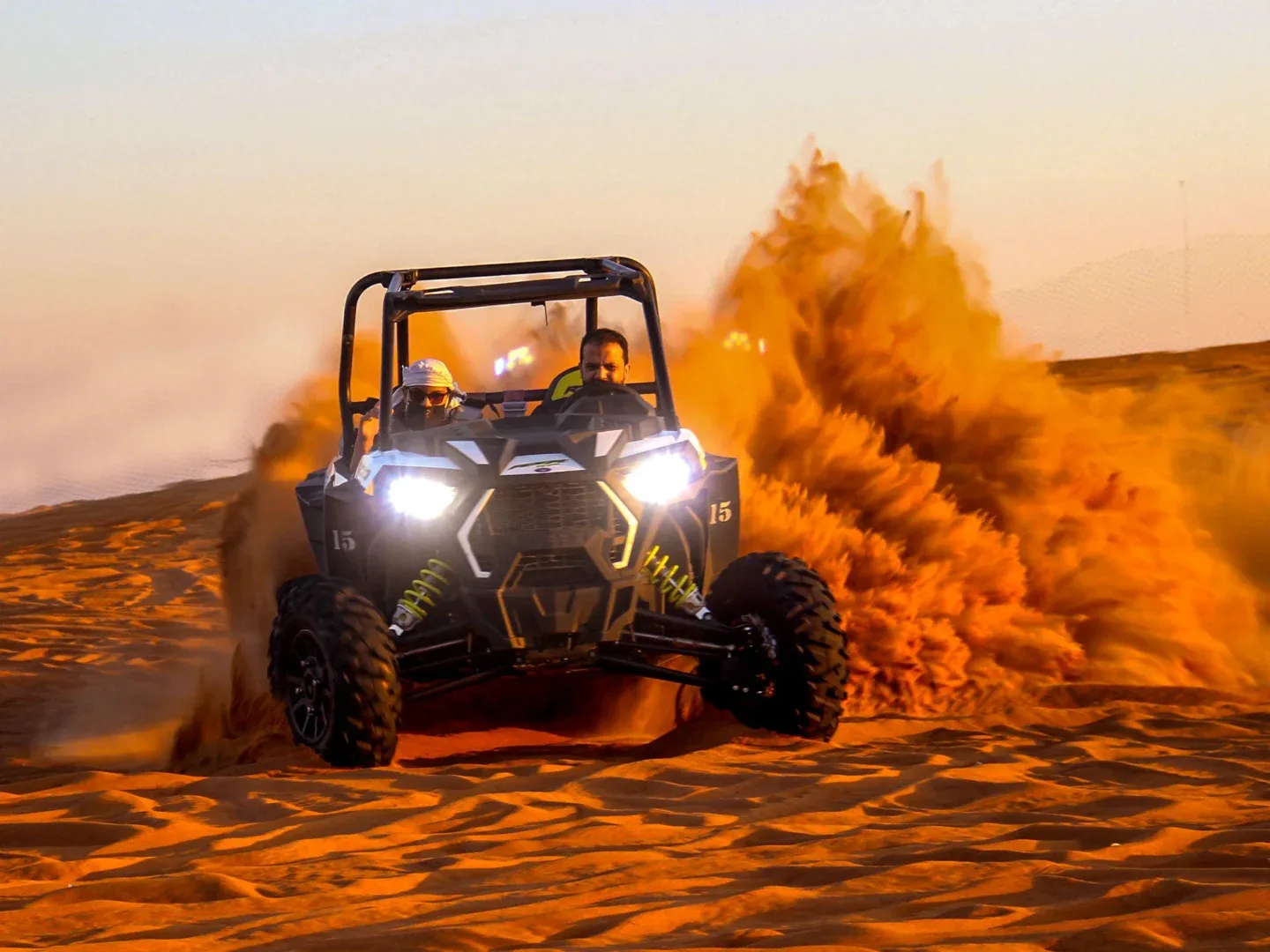 Tourists driving two-seater dune buggies across the vast, golden desert landscape of Dubai under a clear blue sky