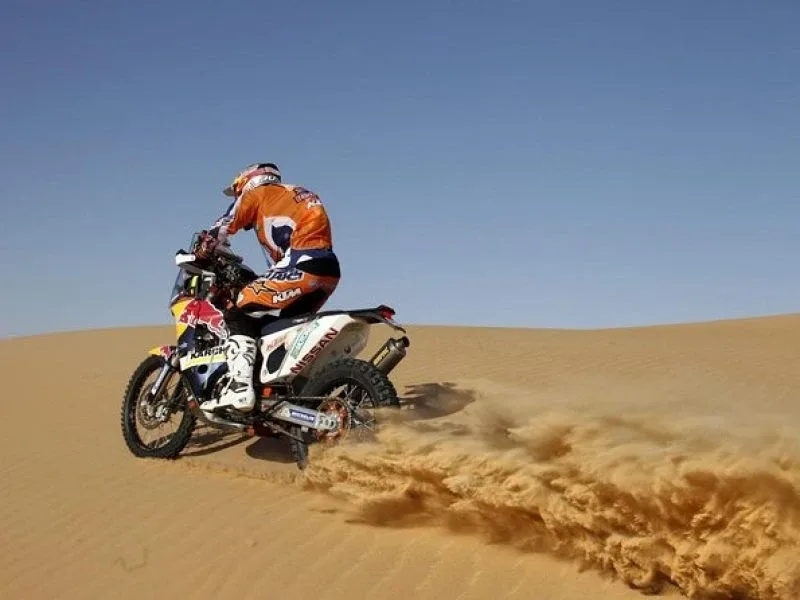 KTM dirt bike rider kicking up sand while speeding across a vast Dubai desert dune at sunset