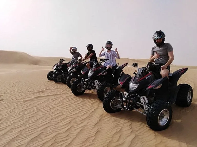 Tourists riding dune buggies across red Dubai dunes at sunset with a hot air balloon in the distance