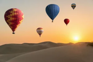 Hot air balloons floating over the Dubai desert at sunrise with the city skyline in the distance, offering a breathtaking view.