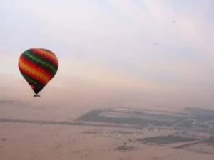 Hot air balloons floating above the Dubai desert at sunrise with the city skyline in the distance, offering breathtaking views