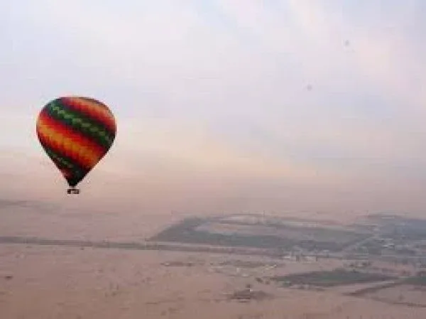 Hot air balloons floating above the Dubai desert at sunrise with the city skyline in the distance, offering breathtaking views