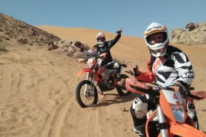 KTM dirt bikes parked in a row in the Dubai desert with a rider in full gear standing next to one
