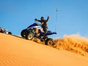 Tourists riding ATVs across the vast golden sand dunes of Dubai desert under a clear blue sky