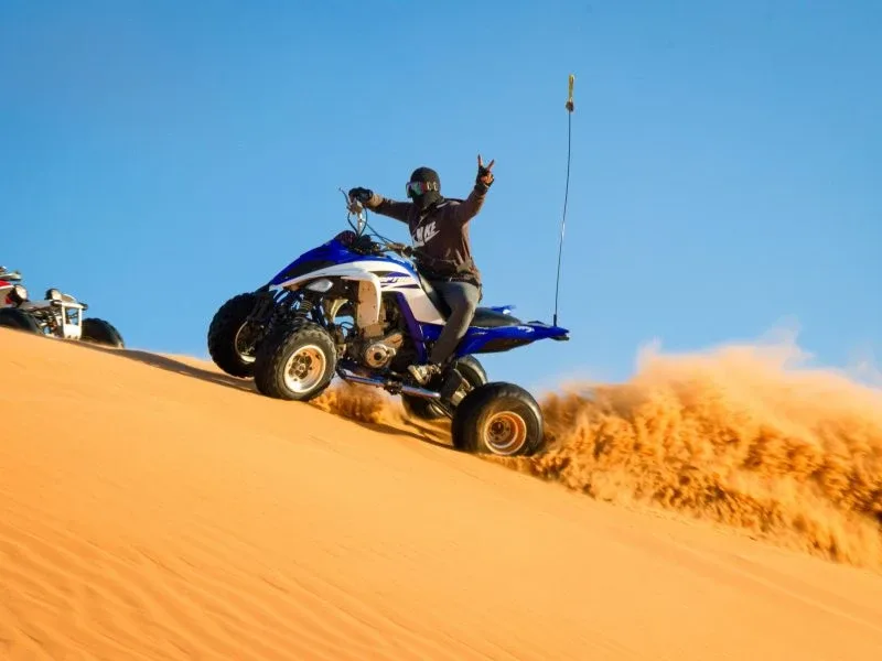 Tourists riding ATVs across the vast golden sand dunes of Dubai desert under a clear blue sky