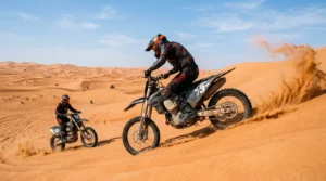 Rider on a rented dirt bike climbing an orange dune with a guide behind during a bike rental in Dubai