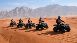 Helmeted riders following a guide on a quad bike desert safari in Ras Al Khaimah with mountains behind