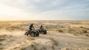 Two riders on quad bikes crossing pale sand dunes and steppe grass in Russia's Astrakhan desert at sunrise